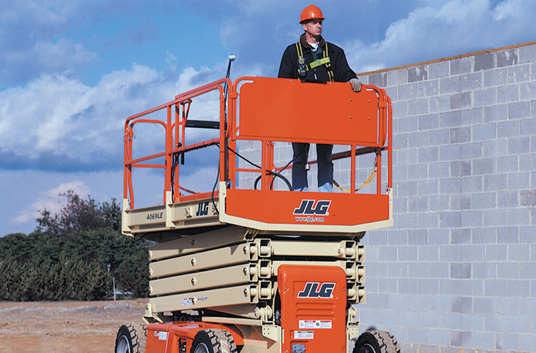 Trabajador realizando un trabajo en altura con un elevador tijera JLG tipo Genie distribuidas por OZMAQ. La plataforma de altura es ideal para tareas de construcción o mantenimiento, tanto en interiores como en exteriores.